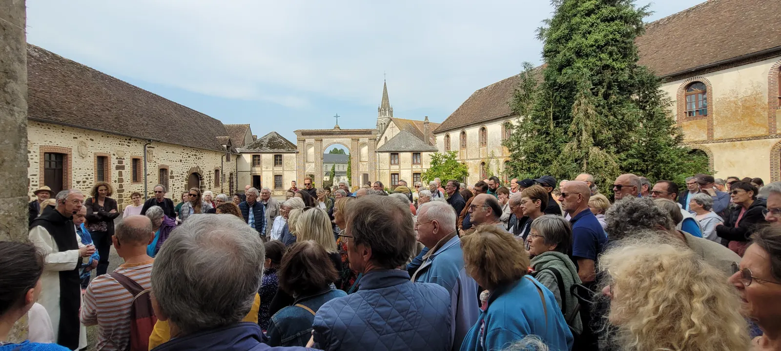 Une foule de visiteurs rassemblés dans la cour de l’abbaye, devant les bâtiments de pierre