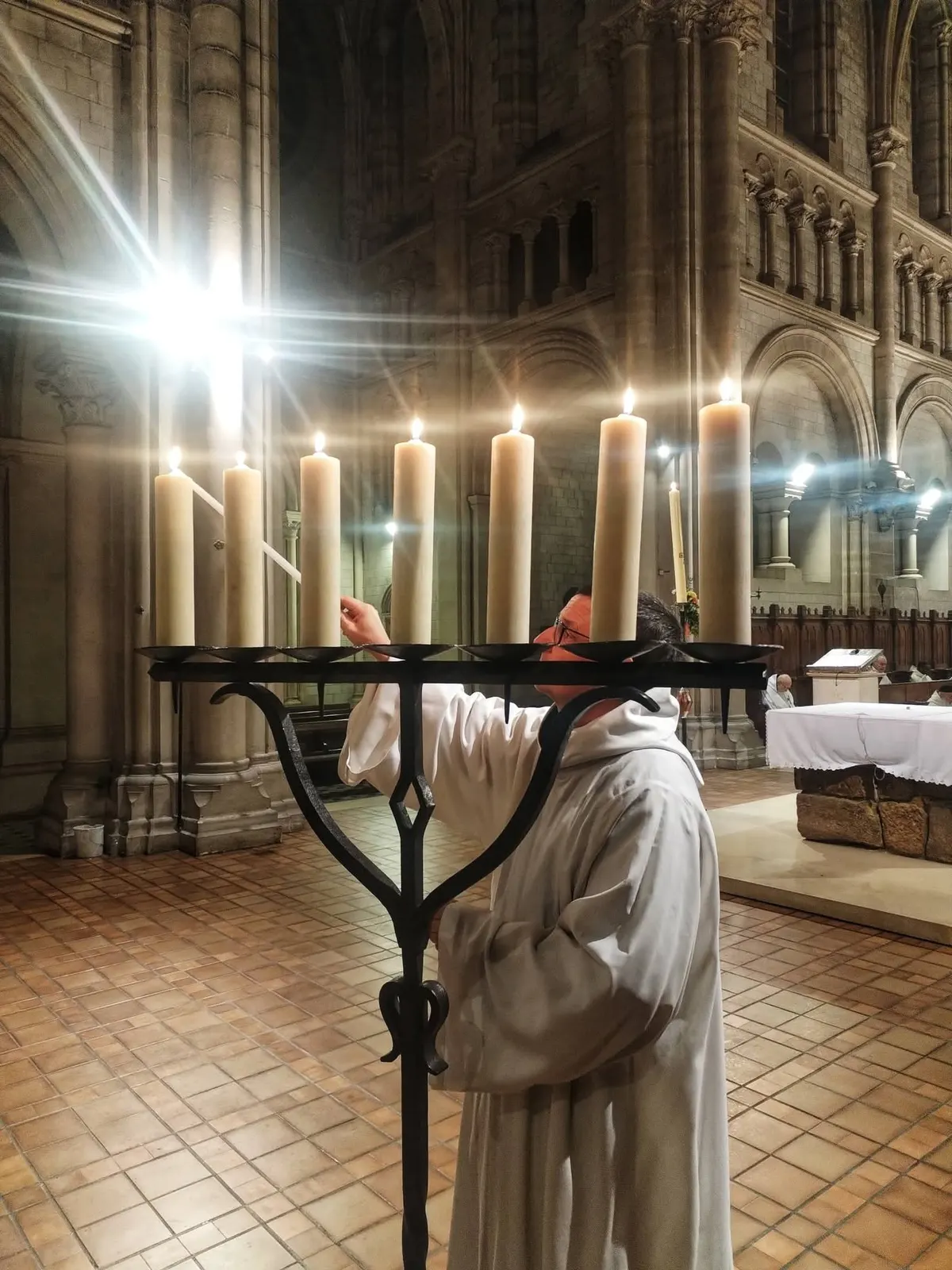 Un moine devant les grands cierges allumés, à contre-jour dans l’église