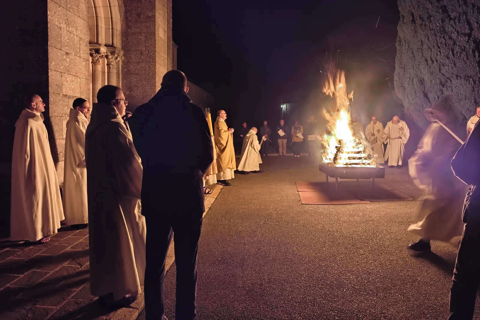 Les moines en coule blanche et les fidèles autour du feu nouveau, dans la nuit, devant les bâtiments de l’abbaye